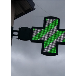 Croix de pharmacie lumineuse à LED verte et blanche fixée sur une façade de bâtiment.