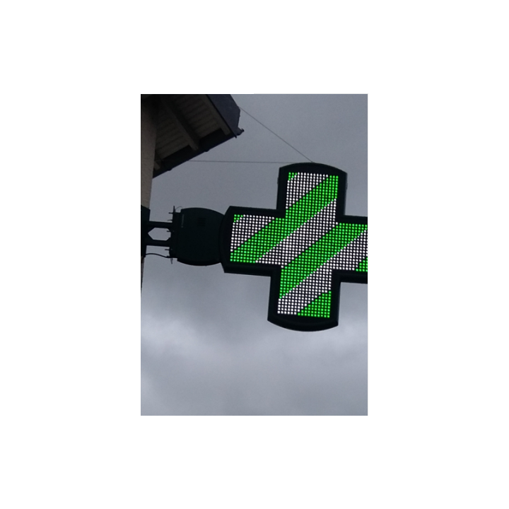 Croix de pharmacie lumineuse à LED verte et blanche fixée sur une façade de bâtiment.