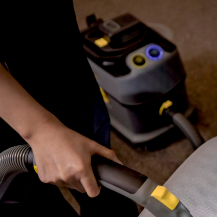 image d'une main qui tient le flexible de l'aspirateur et le corps de l'aspirateur en arrière fond